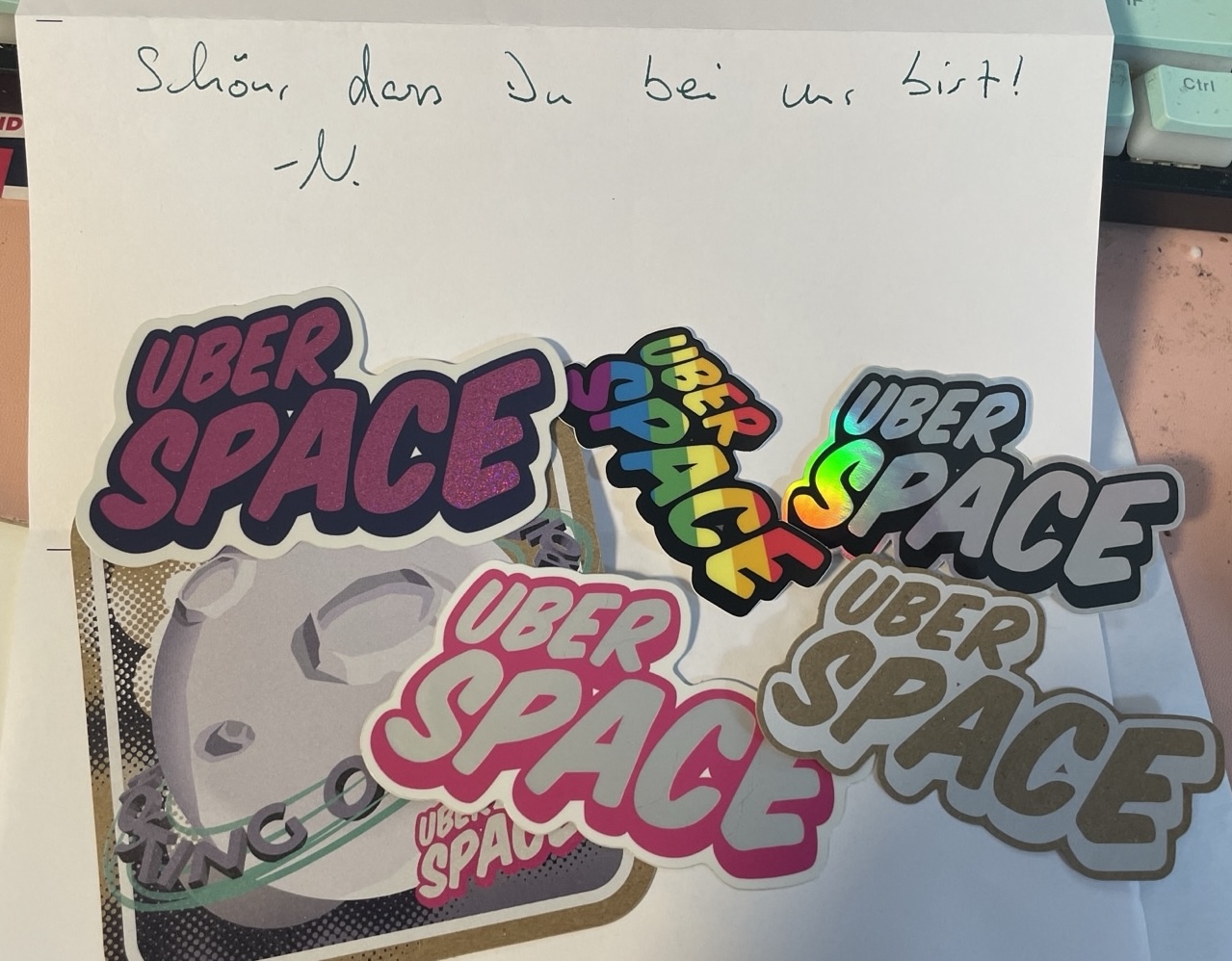 Various stickers with the Uberspace logo on a letter. The letter says in german: “Nice to have you with us! - N”